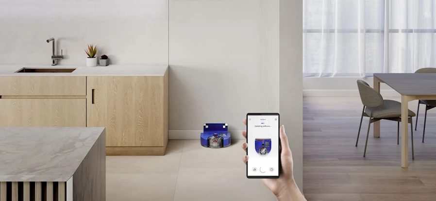 Açıklama: A hand holding a phone with a robot vacuum in the background

Description automatically generated